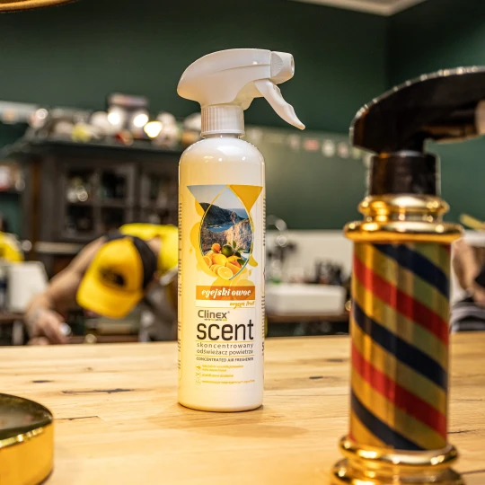 Butelka odświeżacza powietrza Clinex Scent Egejski Owoc stojąca na drewnianym blacie w salonie fryzjerskim.