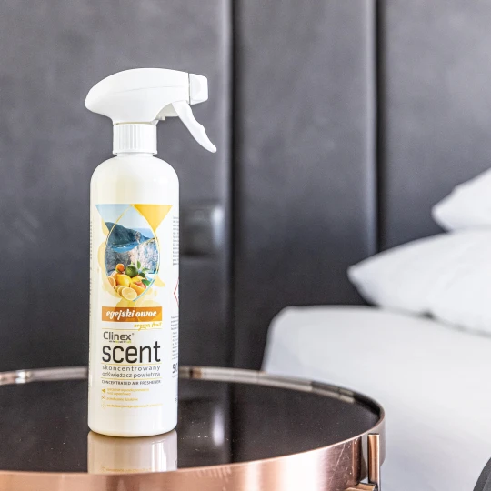 Butelka odświeżacza powietrza Clinex Scent Egejski Owoc, która stoi na szklanym stoliku.