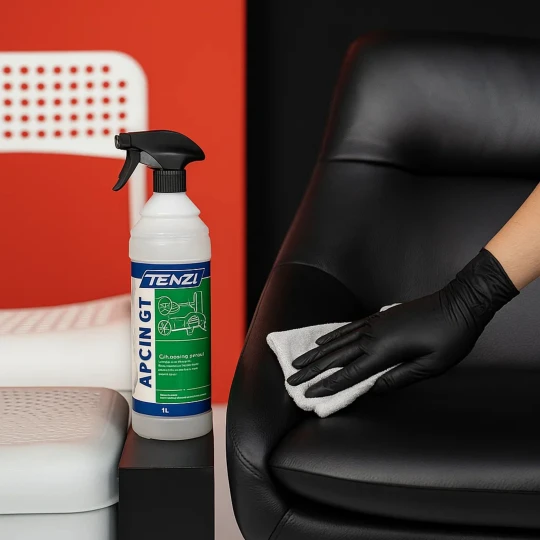 Butelka uniwersalnego środka czyszczącego APC IN GT 1l stoi, podczas gdy w tle ręka w czarnej rękawiczce czyści skórzany fotel, co ukazuje zastosowanie produktu, a obok widoczne jest plastikowe krzesło.