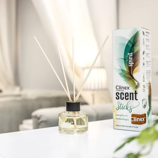 Buteleczka z patyczkami zapachowymi Clinex Scent Spirit stoi na białym blacie w salonie kosmetycznym. W tle widoczne są białe zasłony i szare fotele, co podkreśla, że produkt jest przeznaczony do profesjonalnych wnętrz.