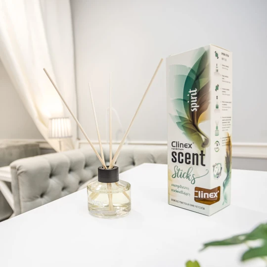 Buteleczka z patyczkami zapachowymi Clinex Scent Spirit stoi na białym blacie w salonie kosmetycznym. W tle widoczne są białe zasłony i szare fotele, co podkreśla, że produkt jest przeznaczony do profesjonalnych wnętrz.