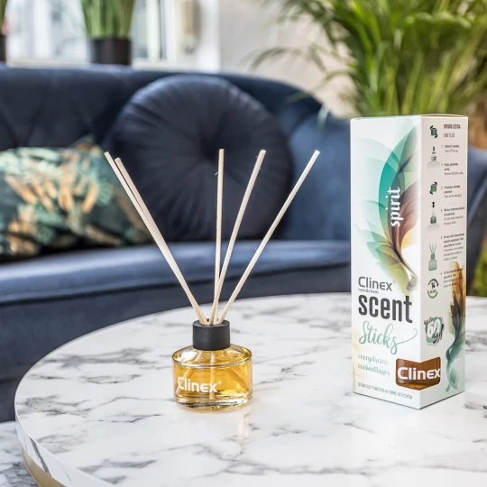 Buteleczka z patyczkami zapachowymi Clinex Scent Spirit stoi na marmurowym stoliku. W tle widoczna jest granatowa sofa i kwiat, co podkreśla, że produkt pasuje do eleganckiego wystroju wnętrz.