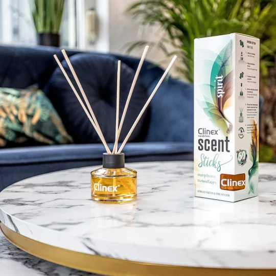 Buteleczka z patyczkami zapachowymi Clinex Scent Spirit stoi na marmurowym stoliku. W tle widoczna jest granatowa sofa i kwiat, co podkreśla, że produkt pasuje do eleganckiego wystroju wnętrz.