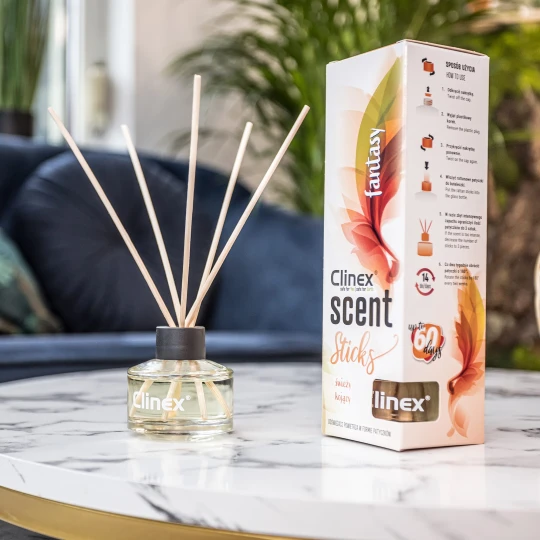 Buteleczka z patyczkami zapachowymi Clinex Scent Fastnasy stoi na marmurowym stoliku. W tle widoczna jest granatowa sofa i kwiat, co tworzy elegancką aranżację wnętrza.