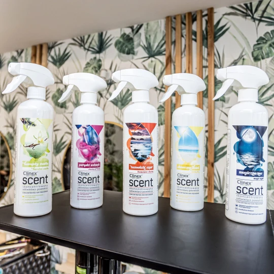 Pięć butelek odświeżacza powietrza Clinex Scent, prezentujących różne warianty zapachowe: Słoneczny Dzień, Magiczna Noc, Paryski Wdzięk, Tasmański Czar oraz Hawajska Wanilia, co podkreśla bogactwo oferty.