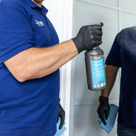 Osoba spryskuje lustro profesjonalnym płynem do mycia i zabezpieczania szkła Clinex Nano Protect Glass 1l, co ukazuje sposób użycia produktu do czyszczenia powierzchni szklanych.