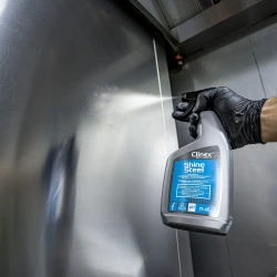 Ręka w rękawiczce używa butelki środka Clinex Shine Steel, spryskując nim zabrudzoną powierzchnię ze stali nierdzewnej, aby ją wyczyścić i nabłyszczyć.