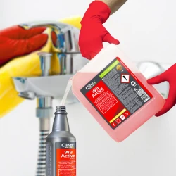 Ręka w czerwonej rękawiczce przelewa skoncentrowany preparat Clinex W3 Active Shield z pięciolitrowego kanistra do mniejszej, jednolitrowej butelki, co ukazuje jego profesjonalne zastosowanie i wydajność.