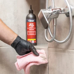 Ręka w czarnej rękawiczce trzyma brudną, różową ściereczkę po czyszczeniu fug, a w tle stoi butelka profesjonalnego preparatu Clinex W3 Fuga, stworzonego do skutecznego usuwania zabrudzeń z fug i spoin.