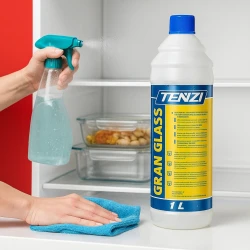 Butelka profesjonalnego płynu do mycia lodówek TENZI Gran Glass 1L stoi, podczas gdy w tle ręka spryskuje wnętrze otwartej lodówki, a następnie wyciera ją szmatką, co ukazuje zastosowanie produktu.