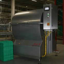 Realistyczna scena w zakładzie przetwórstwa spożywczego: myjka do tacek Traywasher 400 stoi na pierwszym planie, na obudowie widoczna etykieta produktu, w tle regały z wytłaczankami, linia transportowa i stalowe elementy hali, które podkreślają profe