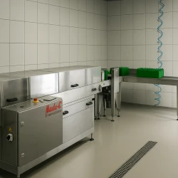 Zdjęcie przedstawia myjkę Inline Traywasher w oryginalnym wyglądzie, ustawioną w poprawionym, realistycznym otoczeniu hali produkcyjnej. Oświetlenie i tło zostały dopracowane, aby całość wyglądała profesjonalnie i oddawała rzeczywiste kolory maszyny.