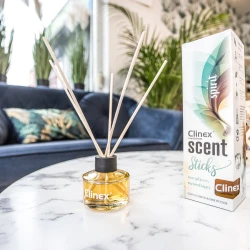 Buteleczka z patyczkami zapachowymi Clinex Scent Spirit stoi na marmurowym stoliku. W tle widoczna jest granatowa sofa i kwiat, co podkreśla, że produkt pasuje do eleganckiego wystroju wnętrz.
