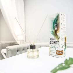 Buteleczka z patyczkami zapachowymi Clinex Scent Spirit stoi na białym blacie w salonie kosmetycznym. W tle widoczne są białe zasłony i szare fotele, co podkreśla, że produkt jest przeznaczony do profesjonalnych wnętrz.