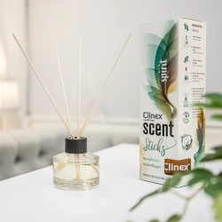 Buteleczka z patyczkami zapachowymi Clinex Scent Spirit stoi na białym blacie w salonie kosmetycznym. W tle widoczne są białe zasłony i szare fotele, co podkreśla, że produkt jest przeznaczony do profesjonalnych wnętrz.