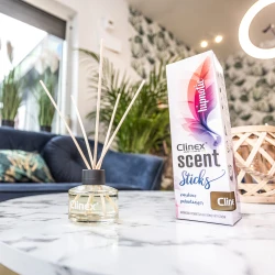 Buteleczka z patyczkami zapachowymi Clinex Scent Hipnotic stoi na marmurowym stoliku obok drewnianego świecznika. W tle widoczna jest granatowa sofa i kwiat, co tworzy elegancką aranżację wnętrza.
