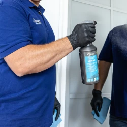 Osoba spryskuje lustro profesjonalnym płynem do mycia i zabezpieczania szkła Clinex Nano Protect Glass 1l, co ukazuje sposób użycia produktu do czyszczenia powierzchni szklanych.