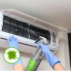 Ręka w niebieskiej rękawiczce spryskuje wnętrze klimatyzacji preparatem CLINEX Nano Protect Silver Nice 1L, co ukazuje jego zastosowanie do dezynfekcji. W lewym dolnym rogu zdjęcia widoczny jest przekreślony obrazek wirusa, co symbolizuje działanie a