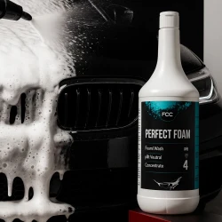Butelka aktywnej piany do mycia samochodów FCC Perfect Foam o pojemności 1 litra stoi przed czarnym autem, które jest myte, co ukazuje zastosowanie produktu.