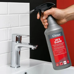 Osoba używa butelki preparatu do mycia łazienek Clinex W3 Sanit o pojemności 1 litra, spryskując umywalkę, co ukazuje przeznaczenie produktu do czyszczenia sanitariatów.