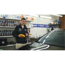 Mężczyzna stoi przed samochodem, trzymając w ręku butelkę quick detailera kwarcowego TENZI Detailer Quartz Spray oraz miękką ściereczkę, co symbolizuje przygotowanie do szybkiego nabłyszczania i zabezpieczania lakieru.